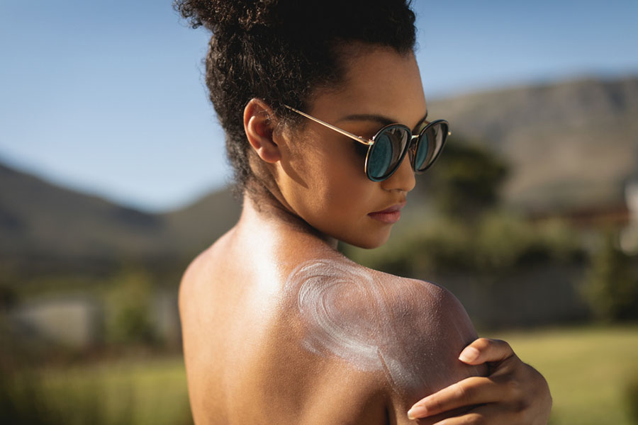 Side view of young mixed race woman applying sunscreen on shoulders in backyard of home on a sunny day
